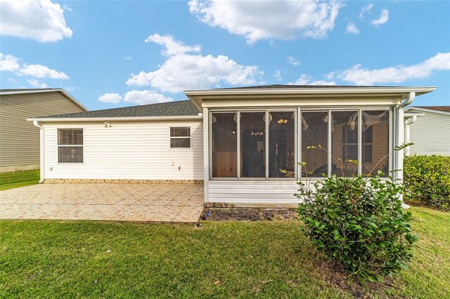 rear view of house featuring a patio, a lawn, and a sunroom