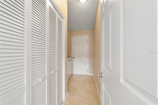 corridor with a textured ceiling, baseboards, and light tile patterned floors