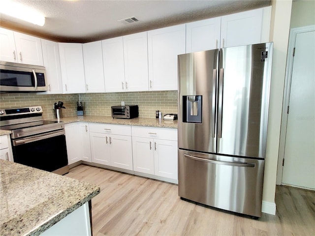 kitchen with light wood-type flooring, white cabinetry, light stone counters, and appliances with stainless steel finishes