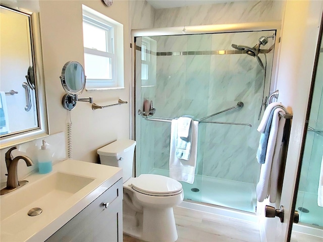 bathroom featuring toilet, vanity, a shower with shower door, and wood-type flooring