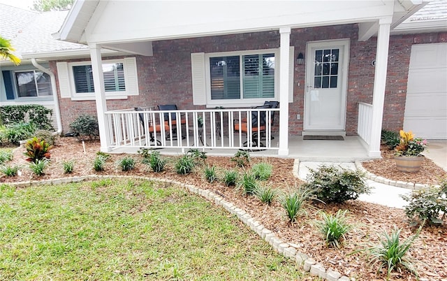 doorway to property with a garage, covered porch, and a yard