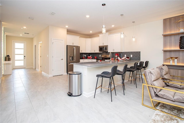 kitchen with a kitchen bar, appliances with stainless steel finishes, kitchen peninsula, pendant lighting, and white cabinets