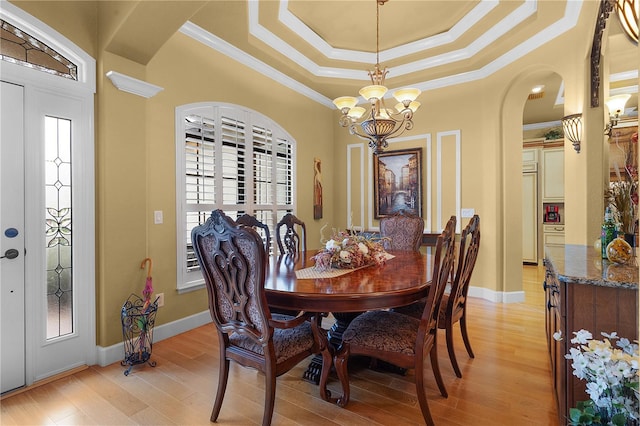 dining room featuring a raised ceiling, ornamental molding, light hardwood / wood-style floors, and an inviting chandelier