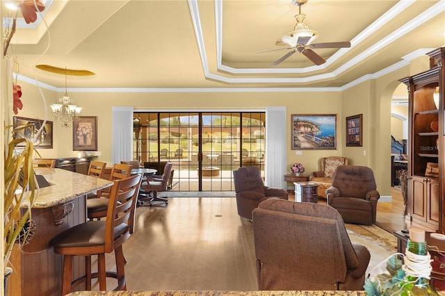 living room featuring a raised ceiling, ceiling fan with notable chandelier, light hardwood / wood-style flooring, and crown molding