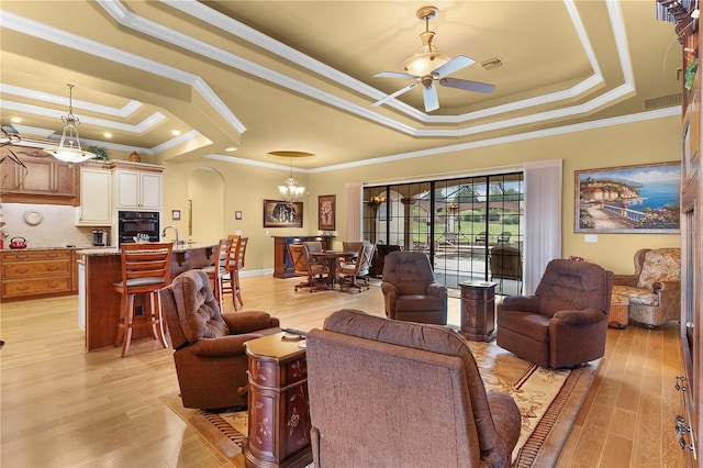 living room with light wood-type flooring, ornamental molding, and a tray ceiling