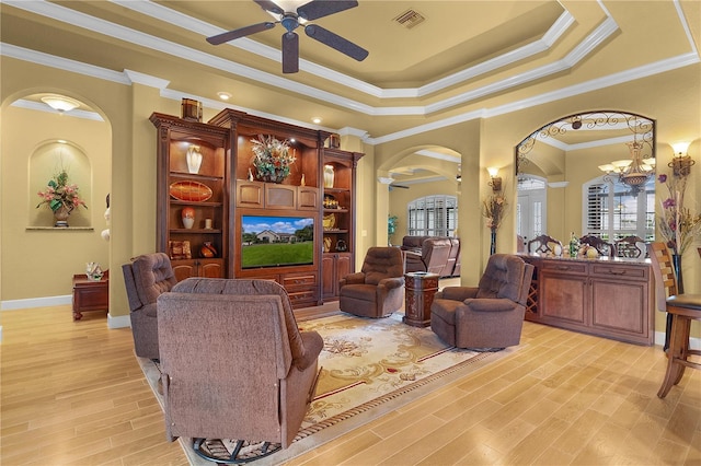 living room with ceiling fan with notable chandelier, light wood-type flooring, crown molding, and a tray ceiling