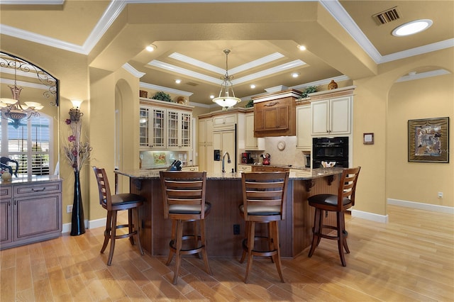 kitchen featuring a center island with sink, paneled built in fridge, crown molding, light stone countertops, and decorative light fixtures