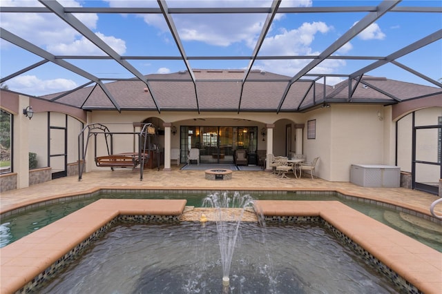 rear view of house with glass enclosure, pool water feature, a patio, and a fire pit