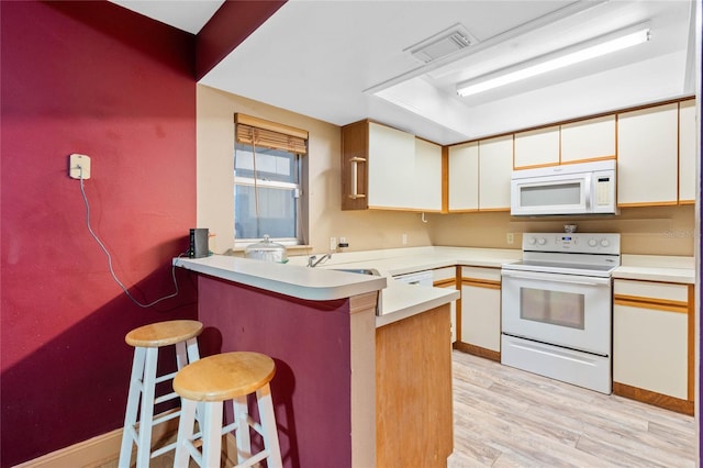 kitchen with kitchen peninsula, white appliances, sink, light hardwood / wood-style flooring, and a breakfast bar area