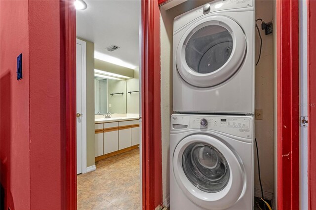 washroom featuring sink, light tile patterned floors, and stacked washing maching and dryer