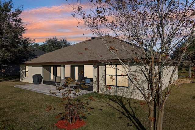 back house at dusk featuring a patio and a lawn