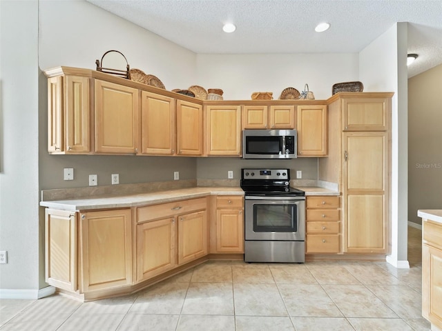 kitchen featuring appliances with stainless steel finishes, light brown cabinets, and a textured ceiling