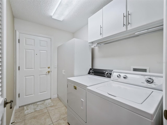 clothes washing area featuring light tile patterned flooring, cabinets, a textured ceiling, and independent washer and dryer