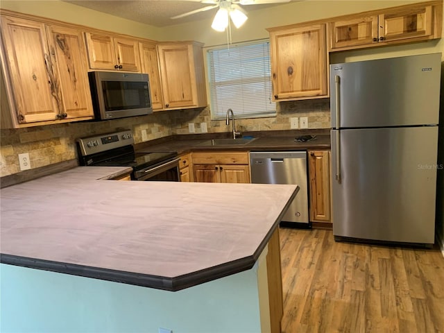 kitchen with appliances with stainless steel finishes, sink, backsplash, light hardwood / wood-style floors, and kitchen peninsula