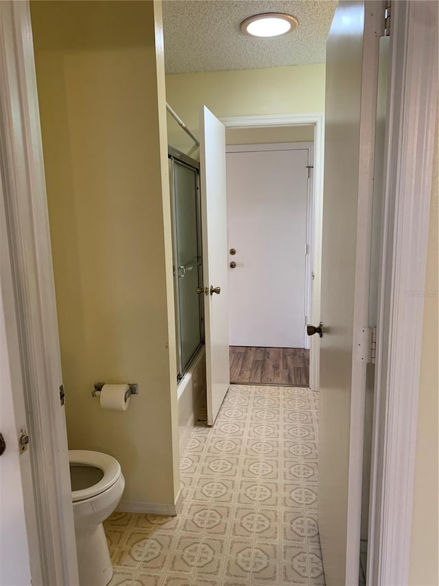 bathroom with toilet, combined bath / shower with glass door, and a textured ceiling