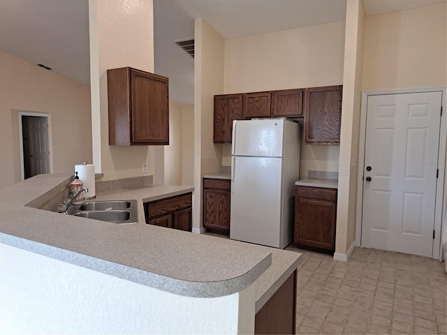 kitchen with kitchen peninsula, white fridge, vaulted ceiling, and sink