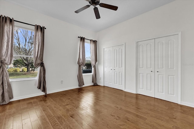 unfurnished bedroom featuring two closets, dark wood-type flooring, and ceiling fan