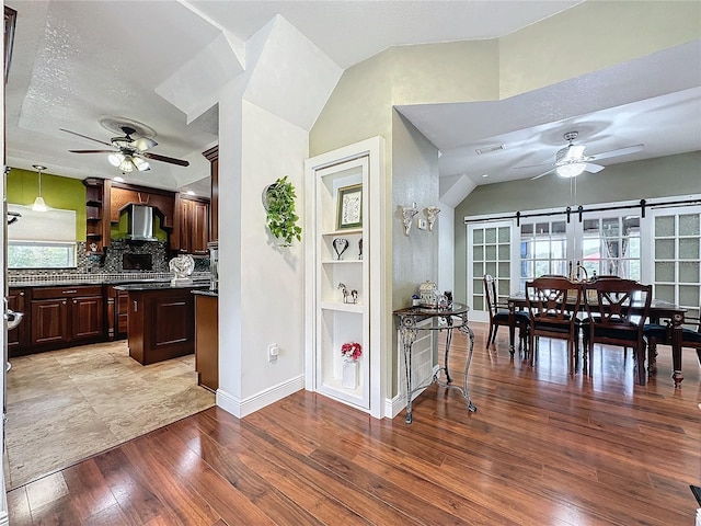 kitchen with ceiling fan, light wood-type flooring, wall chimney range hood, and a barn door