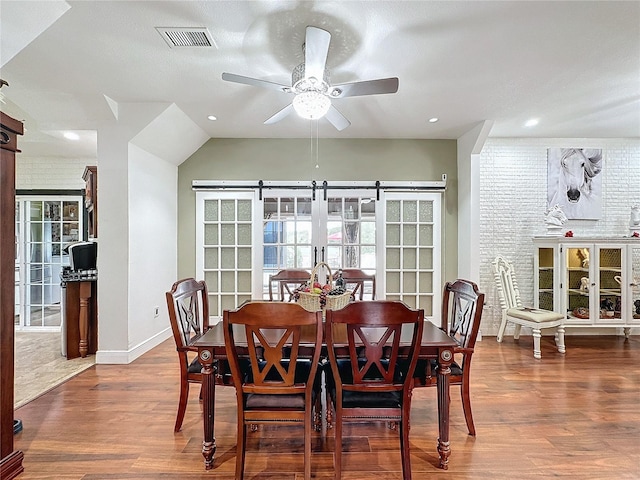 dining room featuring brick wall, ceiling fan, dark wood-type flooring, and a barn door