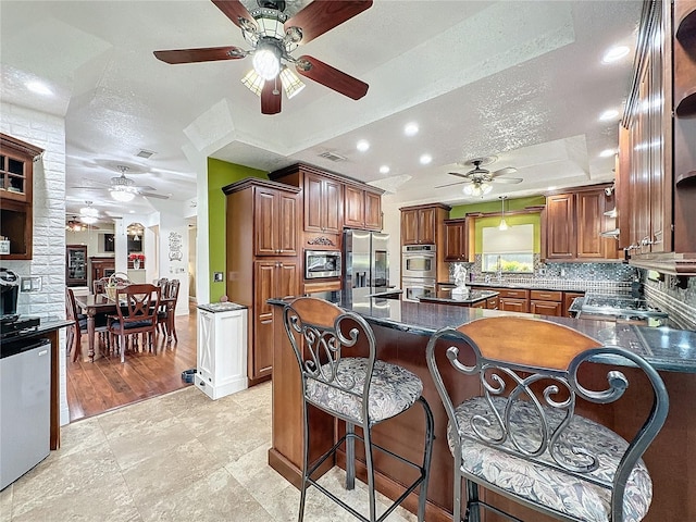 kitchen with stainless steel appliances, ceiling fan, a textured ceiling, a kitchen bar, and decorative backsplash