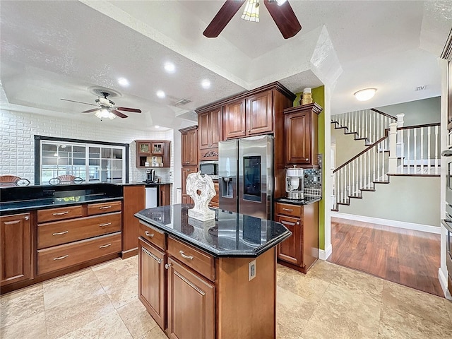 kitchen with stainless steel appliances, a kitchen island, ceiling fan, a textured ceiling, and dark stone countertops