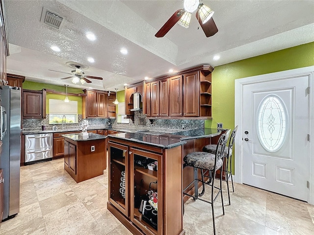 kitchen with a kitchen breakfast bar, wall chimney range hood, a center island, stainless steel fridge, and kitchen peninsula