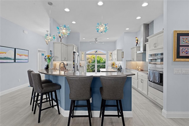 kitchen featuring pendant lighting, wall chimney exhaust hood, ceiling fan, light hardwood / wood-style floors, and stainless steel appliances