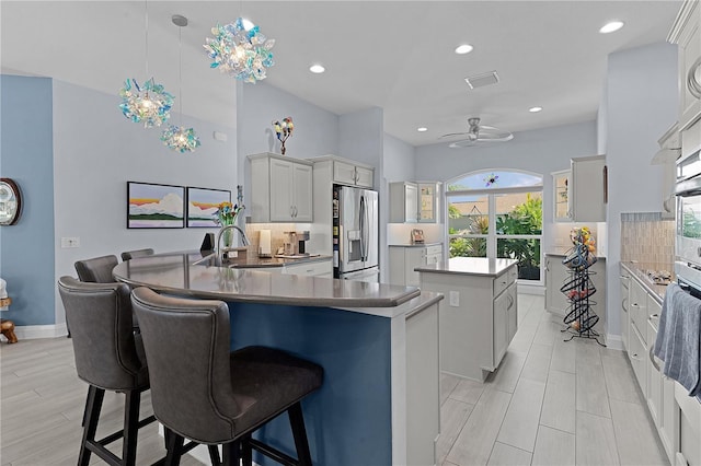 kitchen with stainless steel fridge, backsplash, sink, white cabinetry, and hanging light fixtures