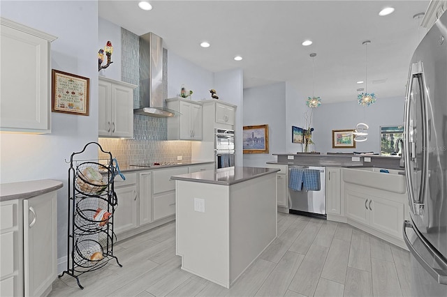 kitchen featuring white cabinetry, wall chimney exhaust hood, pendant lighting, a kitchen island, and appliances with stainless steel finishes