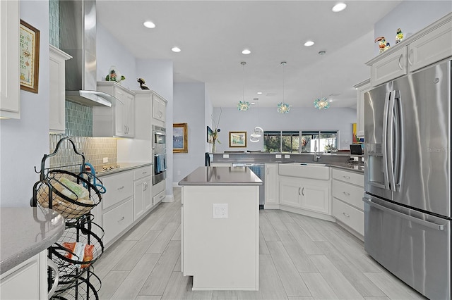 kitchen featuring stainless steel appliances, wall chimney range hood, white cabinets, a kitchen island, and hanging light fixtures