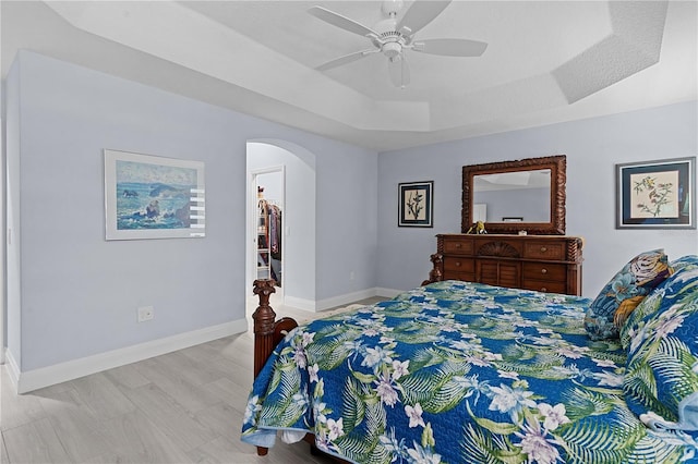 bedroom featuring a walk in closet, ceiling fan, a tray ceiling, light hardwood / wood-style floors, and a closet