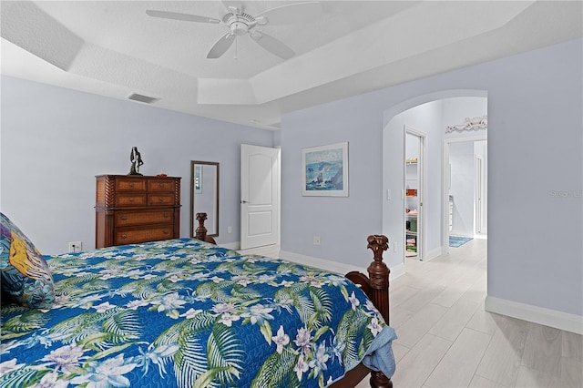 bedroom featuring a raised ceiling, ceiling fan, and a textured ceiling