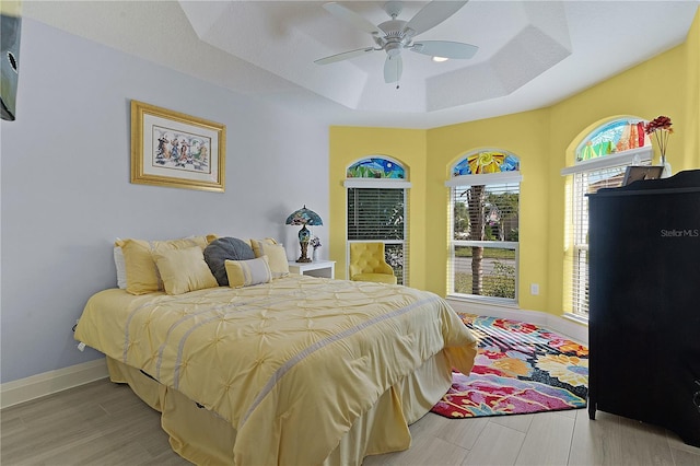 bedroom featuring ceiling fan, light hardwood / wood-style floors, and a raised ceiling