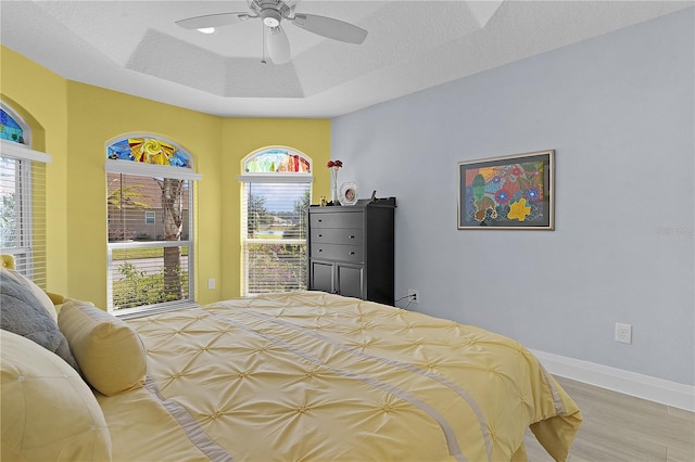 bedroom with a textured ceiling, light wood-type flooring, multiple windows, and ceiling fan