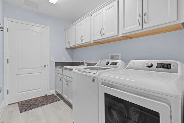 laundry room with a textured ceiling, washer and dryer, cabinets, and sink