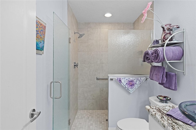 bathroom with a textured ceiling, vanity, toilet, and a shower with shower door