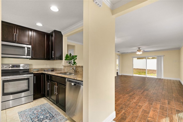 kitchen with light stone countertops, light wood-type flooring, ornamental molding, appliances with stainless steel finishes, and dark brown cabinets