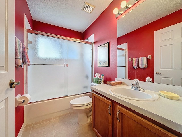 full bathroom featuring combined bath / shower with glass door, vanity, a textured ceiling, tile patterned flooring, and toilet