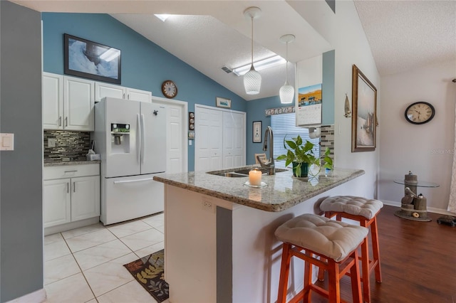 kitchen with sink, white refrigerator with ice dispenser, a textured ceiling, decorative light fixtures, and white cabinets