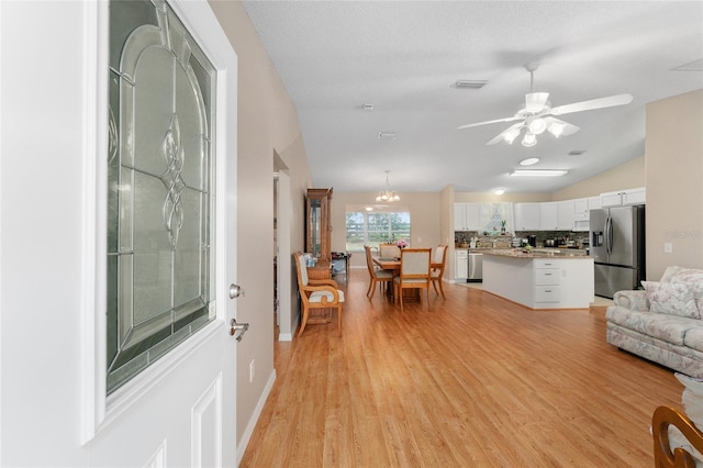 living room featuring a textured ceiling, ceiling fan with notable chandelier, light hardwood / wood-style floors, and vaulted ceiling