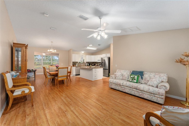 living room featuring ceiling fan with notable chandelier, light wood-type flooring, lofted ceiling, and a textured ceiling