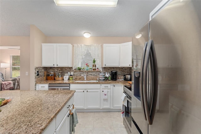 kitchen featuring decorative backsplash, appliances with stainless steel finishes, light stone counters, sink, and white cabinets