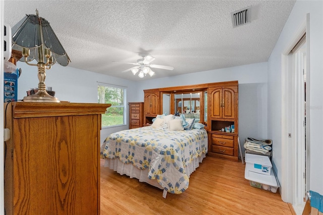 bedroom featuring ceiling fan, light hardwood / wood-style floors, and a textured ceiling