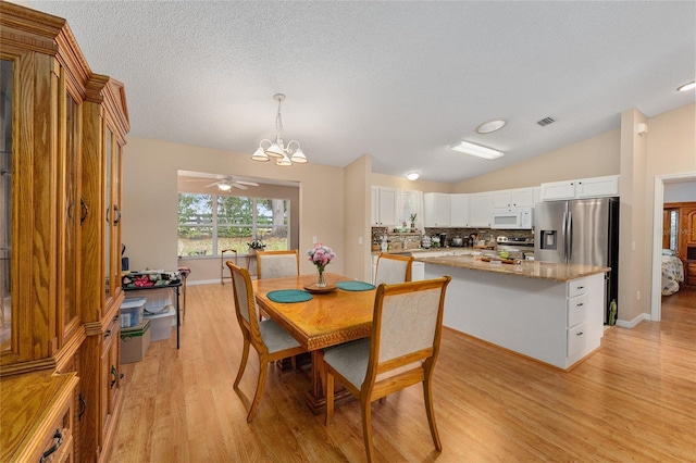 dining room with a textured ceiling, ceiling fan with notable chandelier, light hardwood / wood-style floors, and vaulted ceiling