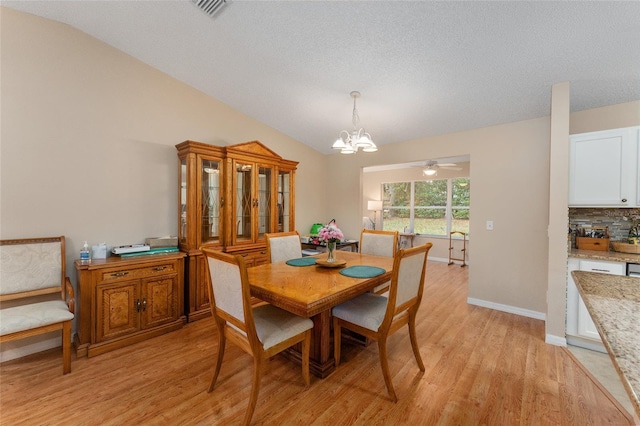 dining room with ceiling fan with notable chandelier, light hardwood / wood-style floors, and vaulted ceiling