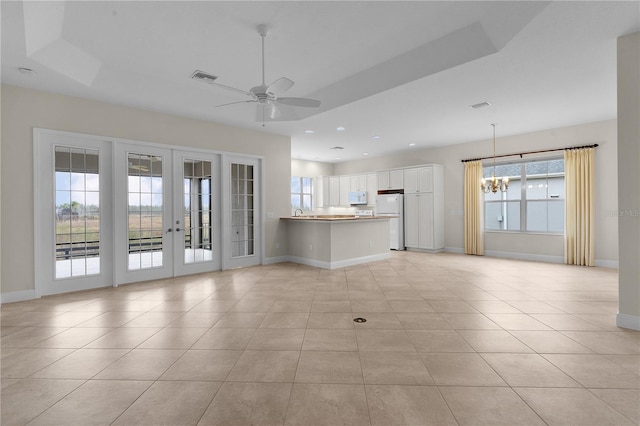 unfurnished living room featuring ceiling fan with notable chandelier, light tile patterned flooring, a raised ceiling, and french doors