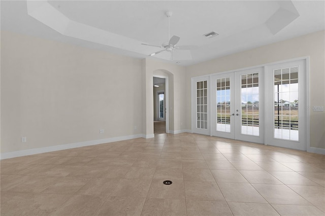 empty room featuring french doors, a tray ceiling, light tile patterned floors, and ceiling fan