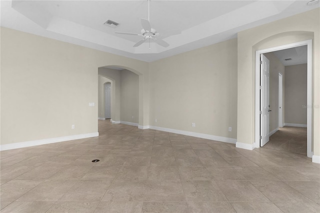 tiled empty room with a raised ceiling and ceiling fan