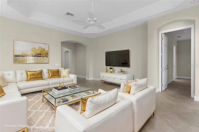 tiled living room with a tray ceiling and ceiling fan