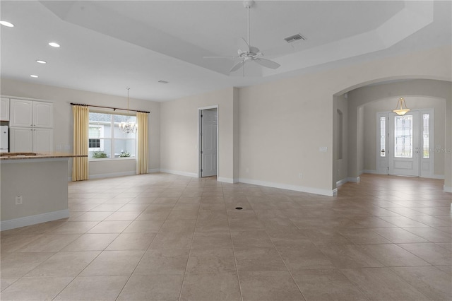 unfurnished living room featuring a raised ceiling, light tile patterned floors, and ceiling fan with notable chandelier